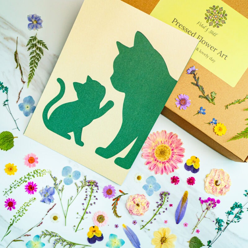 Silhouette of a cat and kitten cutout for pressed flower art, surrounded by colorful real pressed flowers and botanical paper, perfect for nature-inspired craft projects.